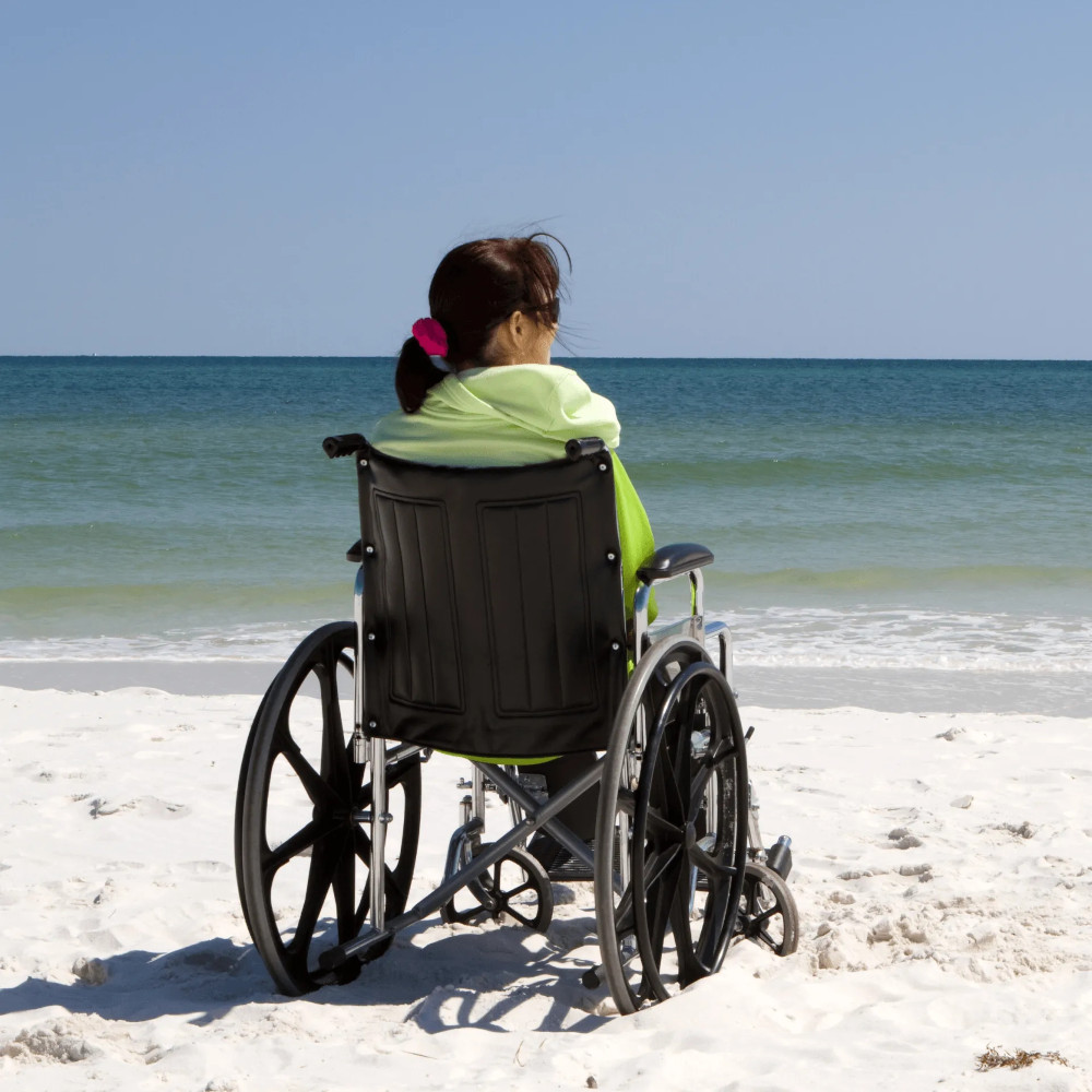 A woman in a wheelchair on a beach looking out over the ocean